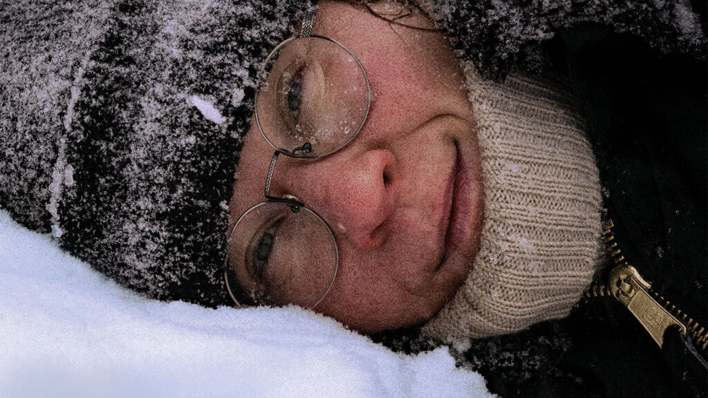 A closeup of poet Sini Silveri looking at the camera in the middle of snowy landscape in Sanni Priha's shortfilm Farewell to Snow – Snowplay.